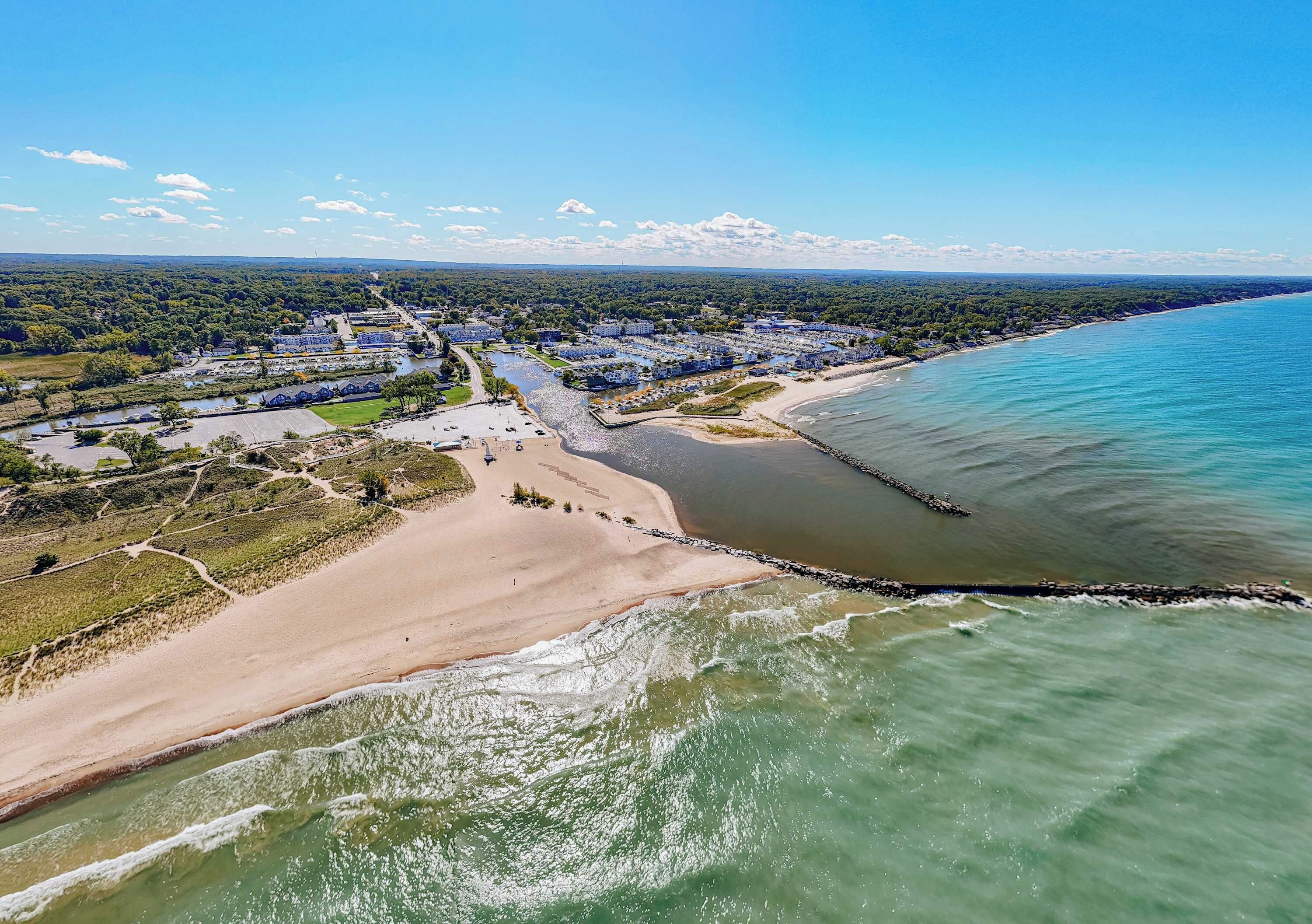 Vue aérienne d’une zone côtière comprenant une plage, un port de plaisance et des immeubles résidentiels.