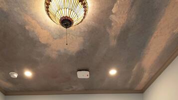 A hotel room with a bed, a ceiling light fixture, and a wall-mounted device.