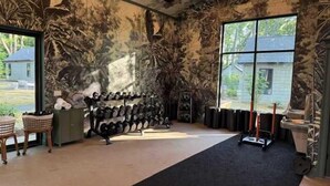 Un gimnasio con equipo de ejercicio, alfombra negra y un ventanal grande.