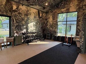 Un gimnasio con equipo de ejercicio, alfombra negra y un ventanal grande.