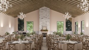 Un gran salón con mesas redondas y sillas de madera, un techo alto de madera y una chimenea con un arreglo floral.
