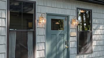 A single-story building with a dark green door, two windows with shutters, and a small porch area.