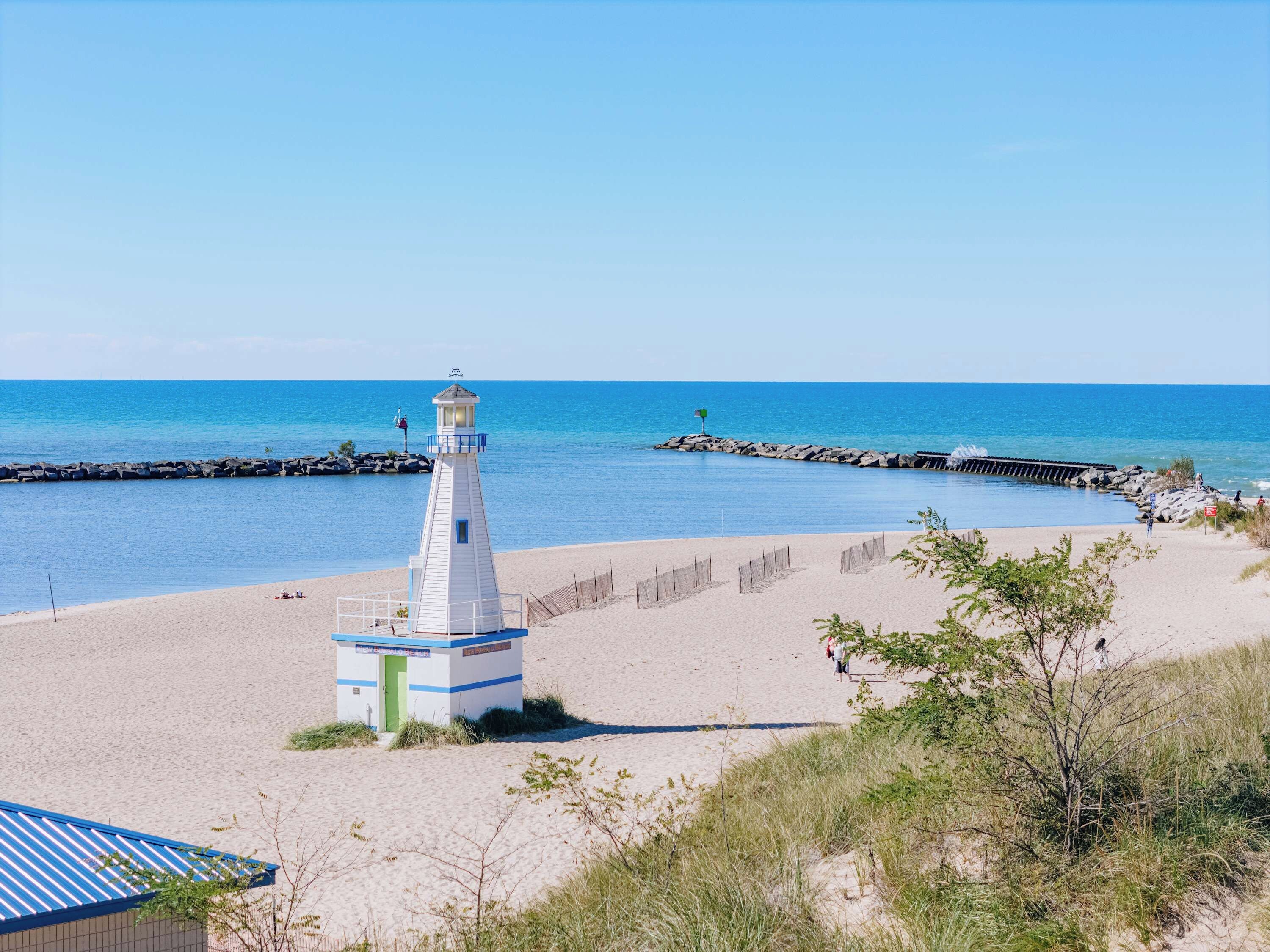 A beach with a lighthouse, clear blue sky, and calm sea.
