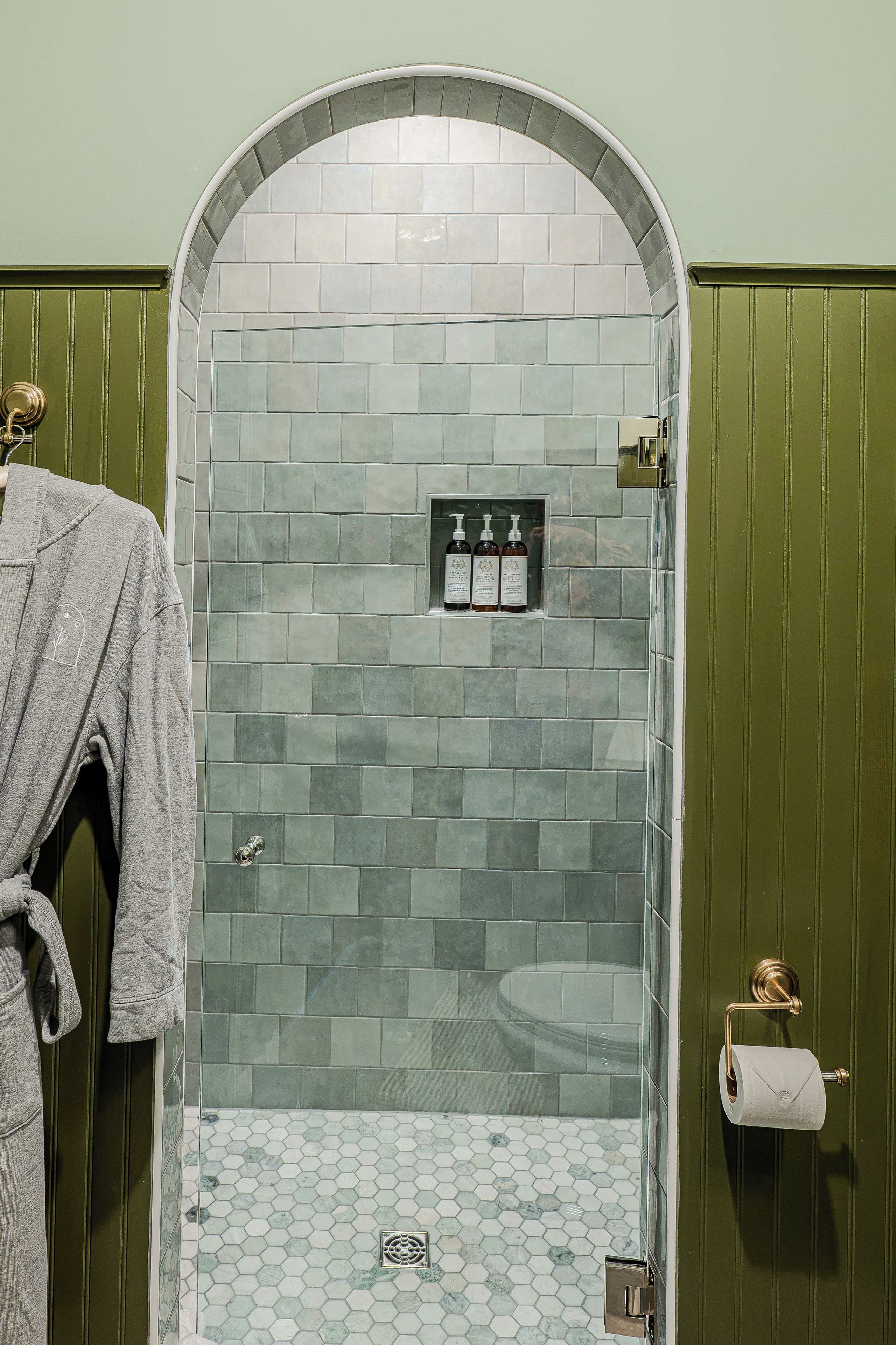 A bathroom with a tiled shower area, a towel rack, and a toilet paper holder.