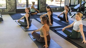A group of people on yoga mats in a room with large windows and exercise equipment.
