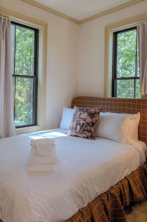 A hotel room with a bed, two windows, and a view of trees.