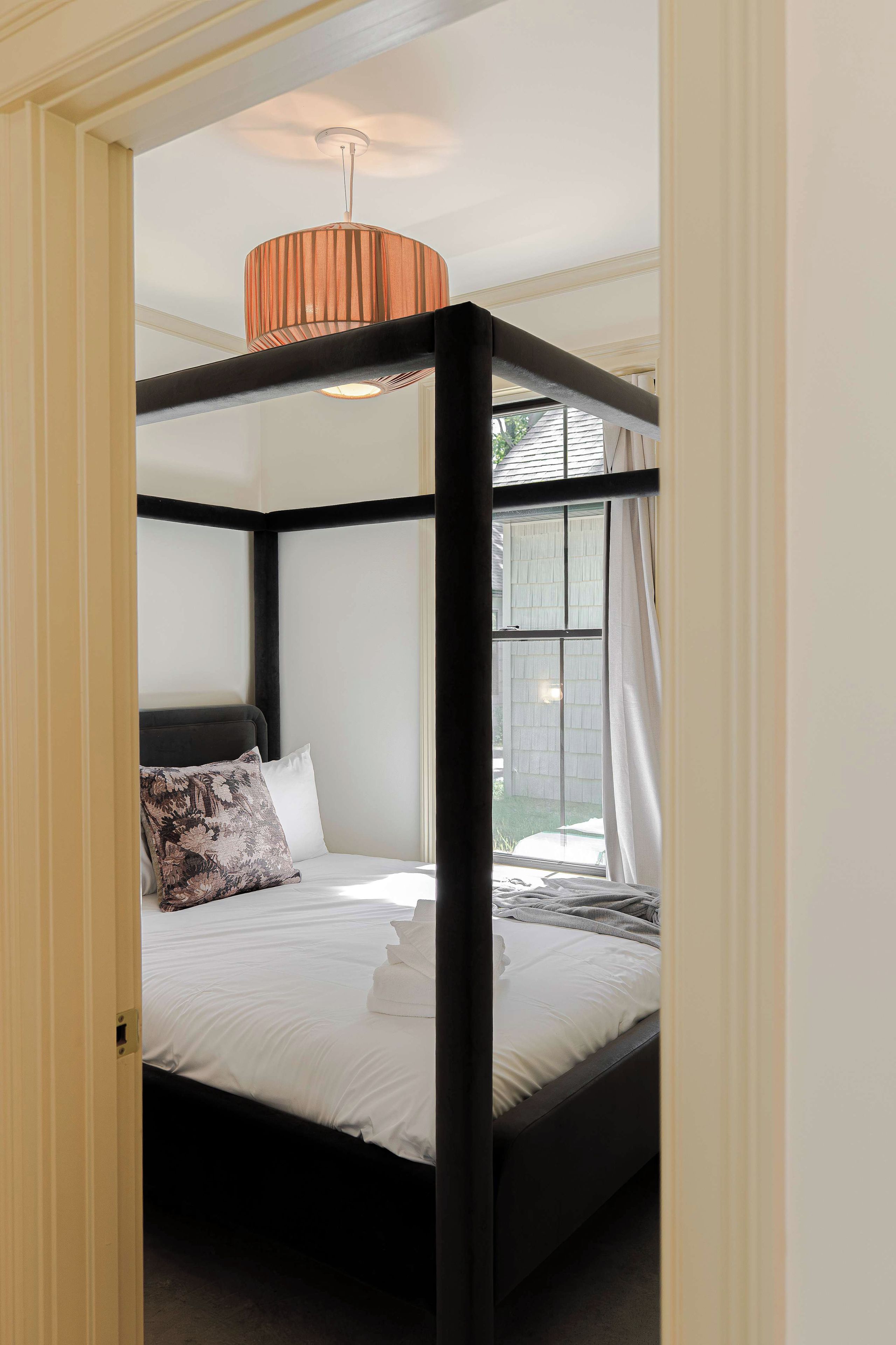 A four-poster bed with a white mattress and pillows, a black frame, and a ceiling light fixture.