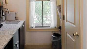A narrow kitchen with a window, a sink, and a trash can.