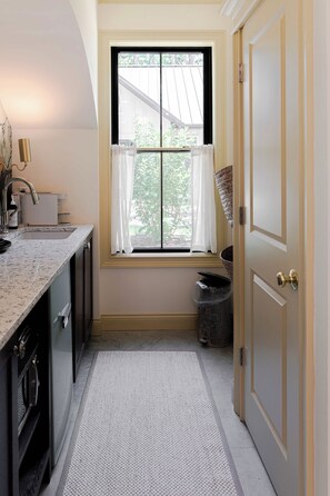 A narrow kitchen with a window, a sink, and a trash can.