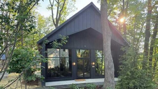 A modern wooden cabin with large windows, surrounded by trees.