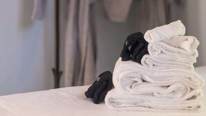 Ordentlich gestapelte Handtücher und Bademäntel auf einem Bett, im Hintergrund ein Metallgestell mit Bademänteln.