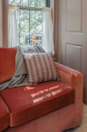 Un sofá de cuero rojo con un cojín estampado y una manta gris en una habitación con ventana y puerta.