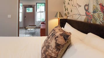 A bedroom with a bed, a nightstand, a lamp, and a door leading to another room.