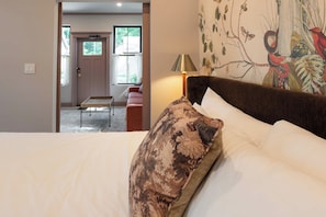 Un dormitorio con una cama, una mesita de noche, una lámpara y una puerta que da a otra habitación.