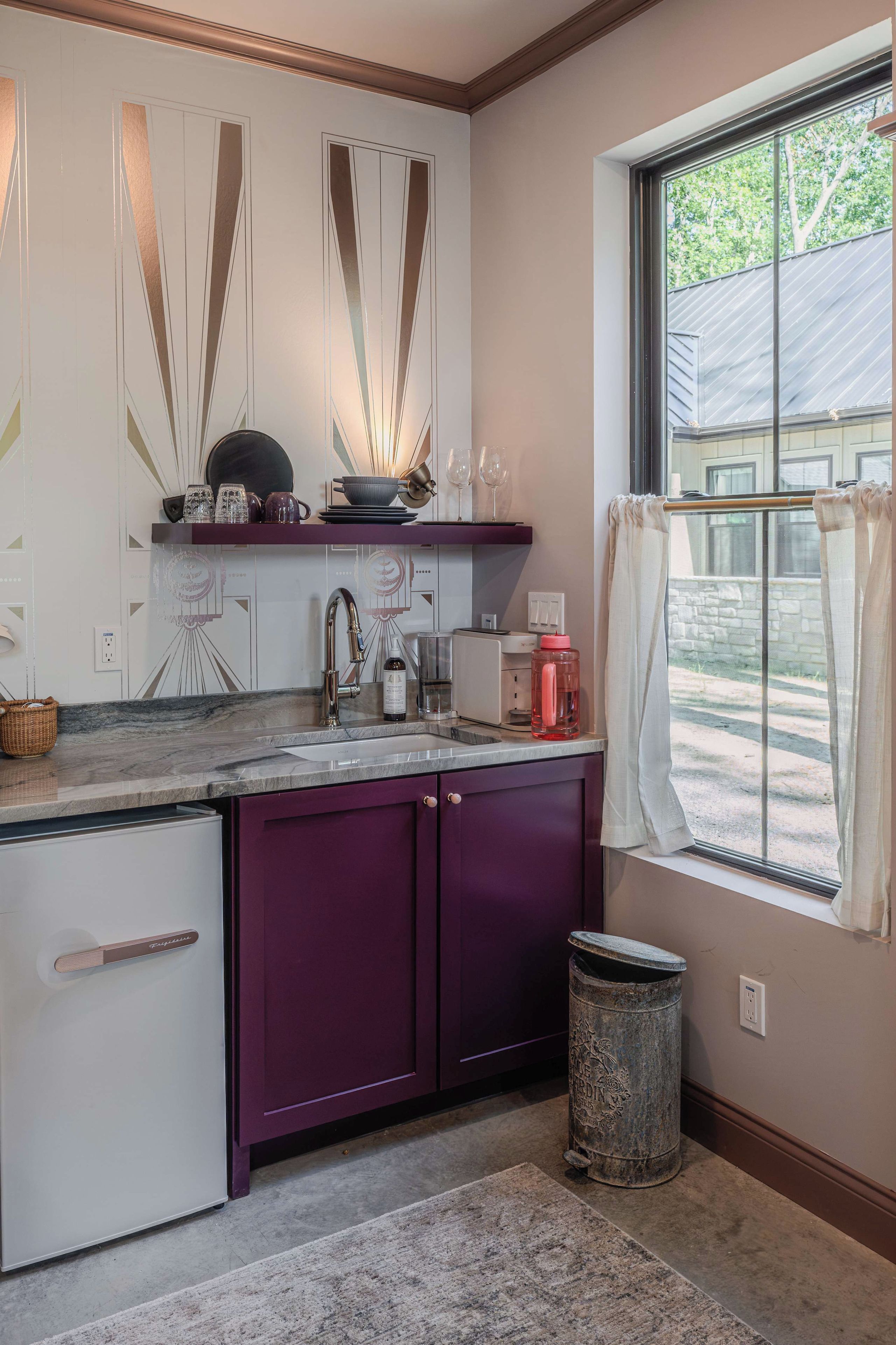 A kitchen with a window, a sink, and a trash can.