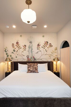 Une chambre à coucher avec un grand lit, deux lampes de chevet, une fresque murale et un luminaire au plafond.