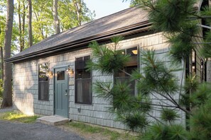A small, single-story building with a shingled exterior, a front door, and two windows.