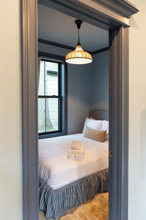 Quarto com cama, almofadas, mesa de cabeceira, janela e luminária pendente.
