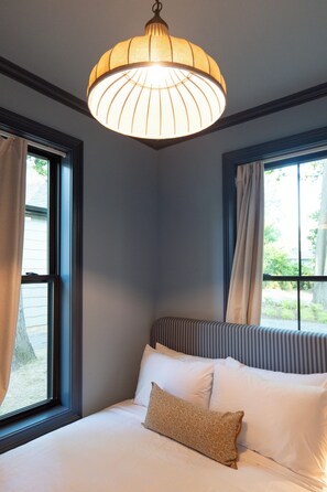 A bedroom with a bed, a window, and a hanging light fixture.