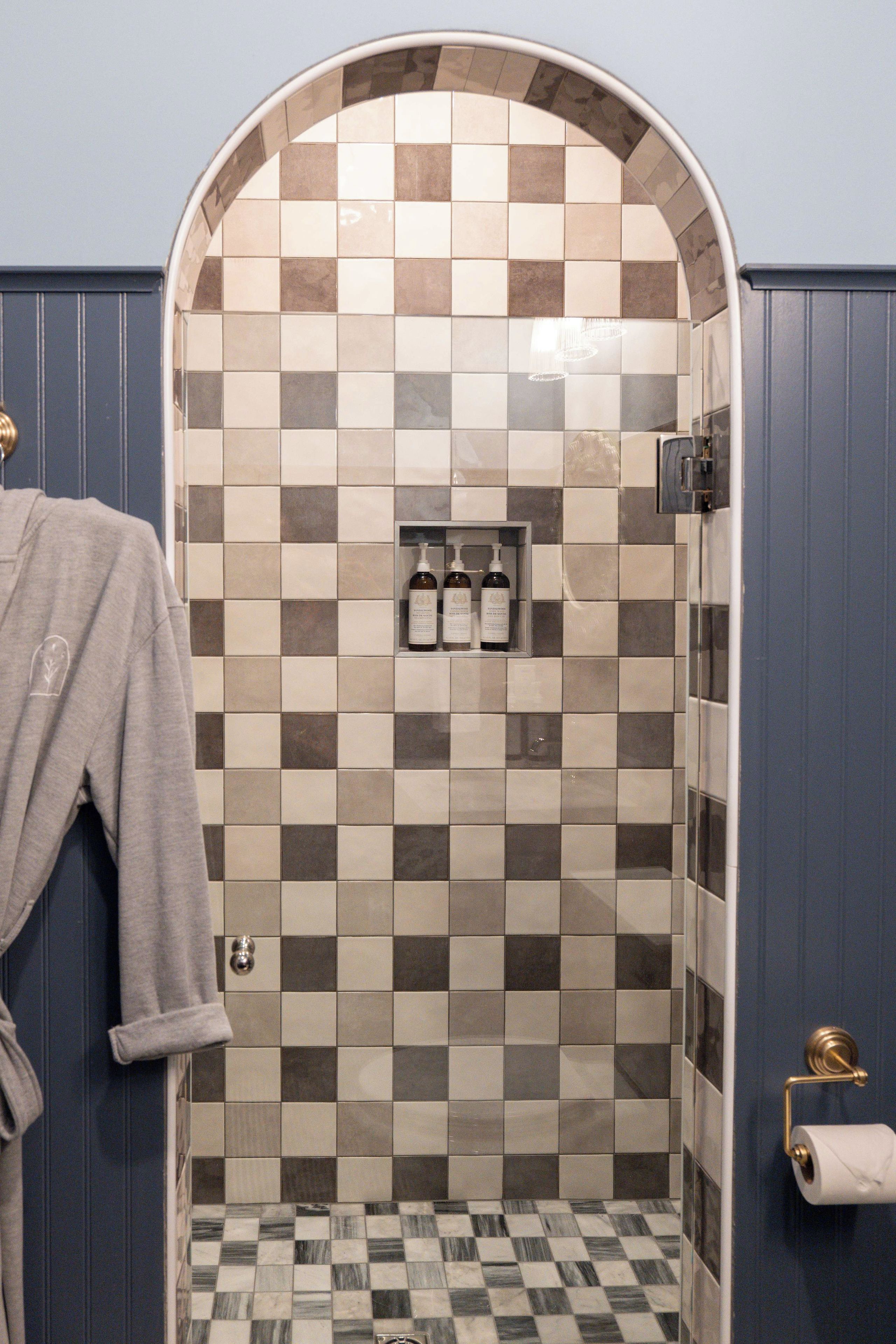 Un baño con pared de baldosas a cuadros, zona de ducha y un perchero.