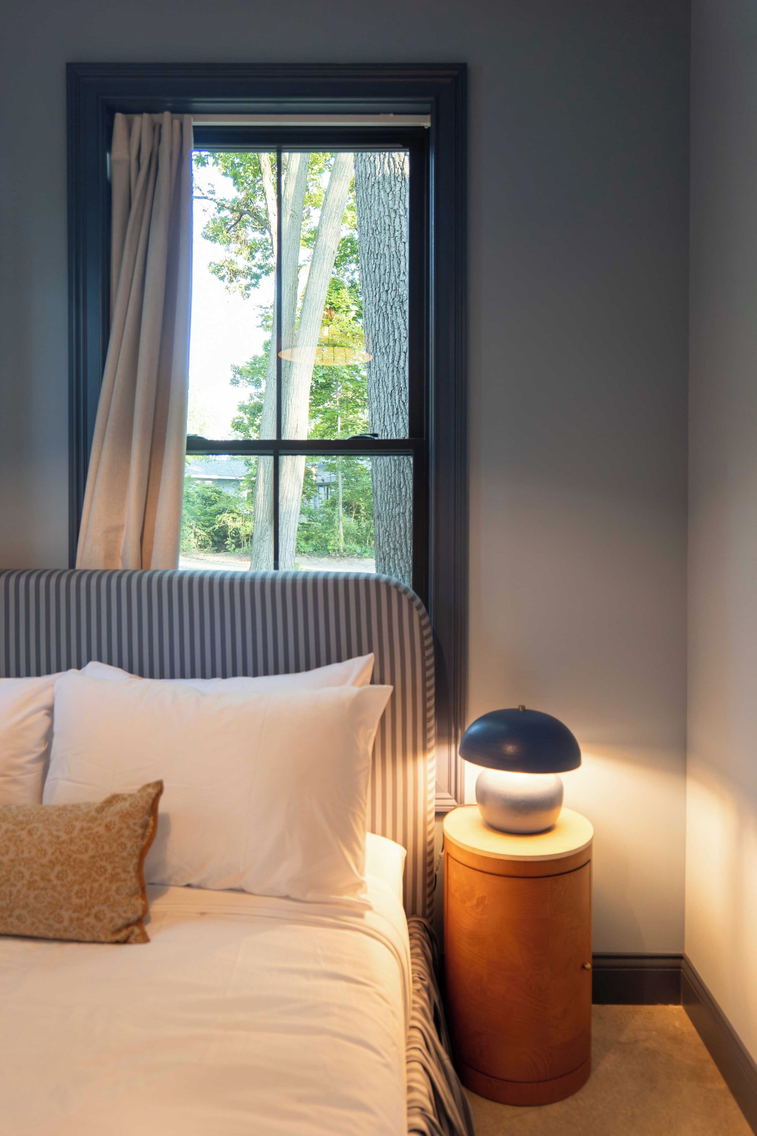 Ein Schlafzimmer mit einem Bett, einer Nachttischlampe und einem Fenster mit Vorhängen.