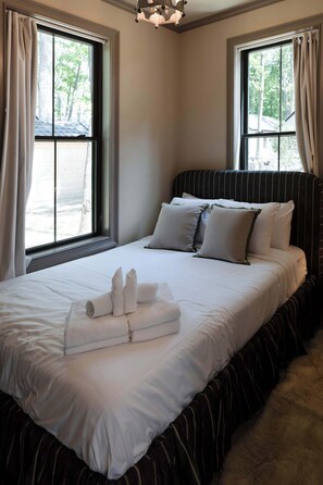 A hotel room with a large bed, two windows, and a view of trees outside.