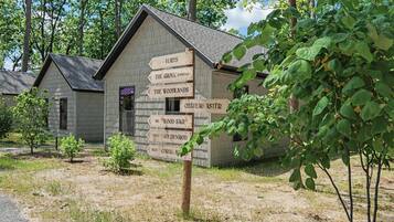 Una cabaña rústica con un cartel de madera que indica lugares cercanos como 'Yurts', 'The Grove (Parking)', 'The Woodlands', 'Chateau Aster', 'Dix Wood Sage', 'Neuf Goldenrod' y 'Huit Coral Bay'.