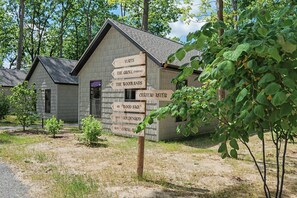 A rustic cabin with a wooden signpost indicating nearby locations such as 'Yurts', 'The Grove (Parking)', 'The Woodlands', 'Chateau Aster', 'Dix Wood Sage', 'Neuf Goldenrod', and 'Huit Coral Bay'.