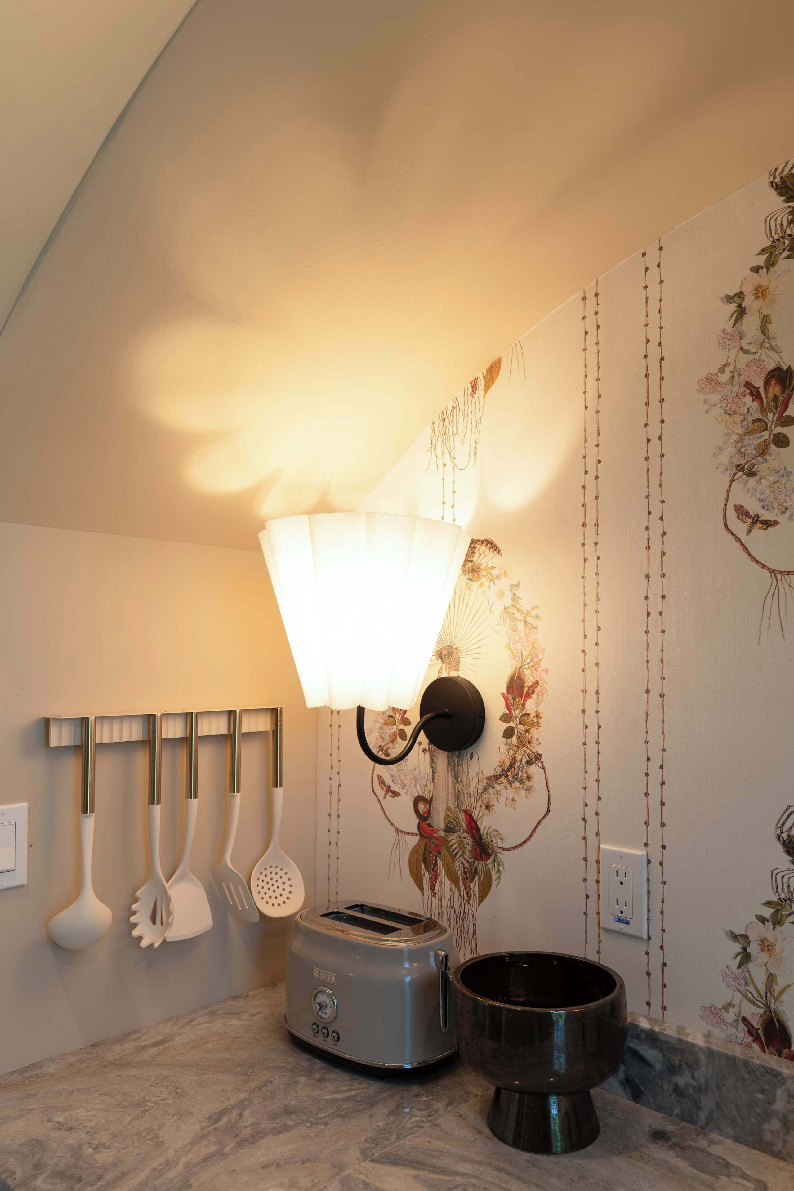 A kitchen with a modern toaster, a black pot, and a wall-mounted lamp.