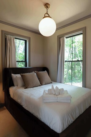 A bedroom with a large bed, two windows with curtains, and a hanging light fixture.