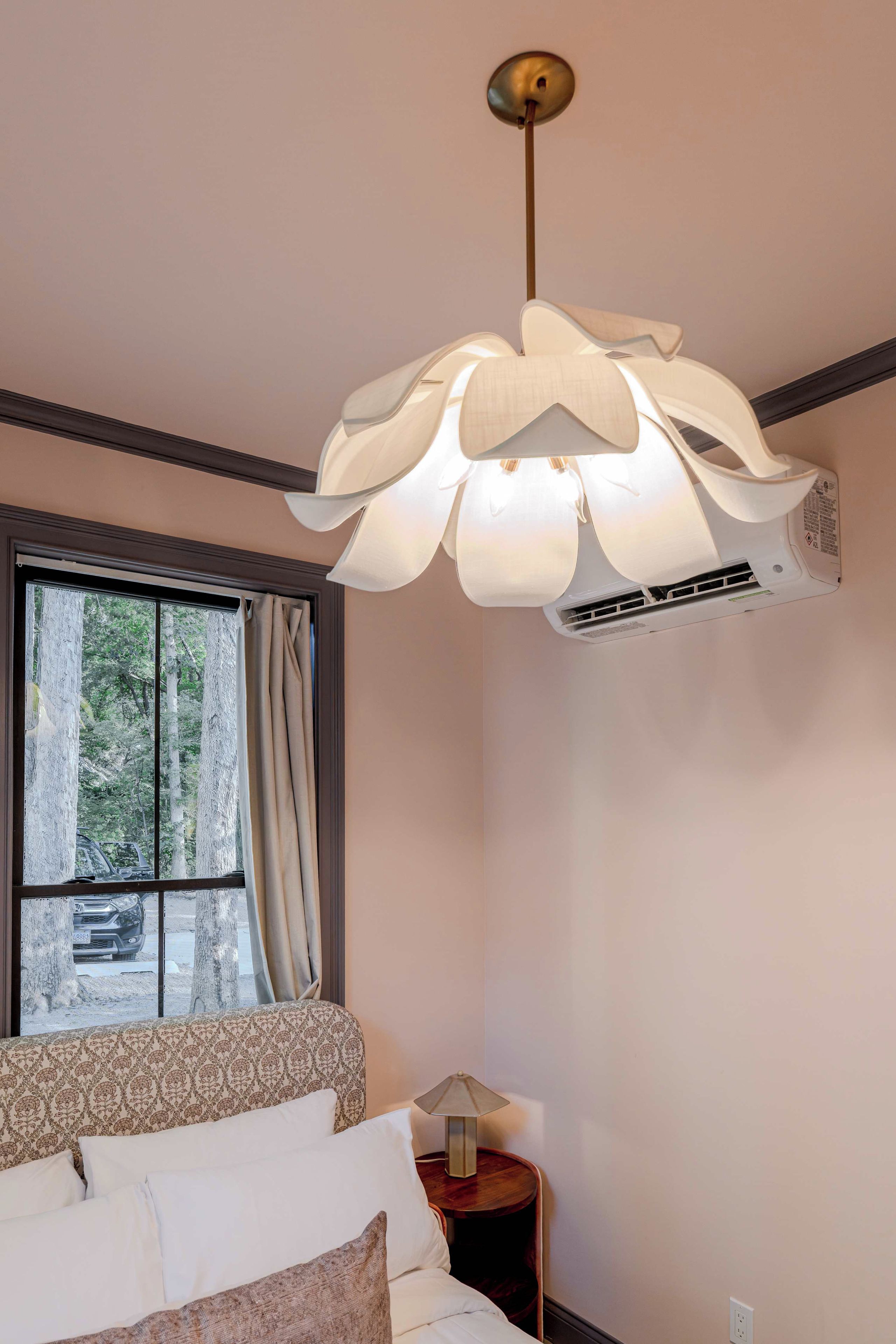 Un dormitorio con cama, ventana con cortinas, equipo de aire acondicionado e iluminación colgante.