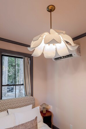 Ett sovrum med en säng, ett fönster med gardiner, en luftkonditioneringsanläggning och en hängande lampa.