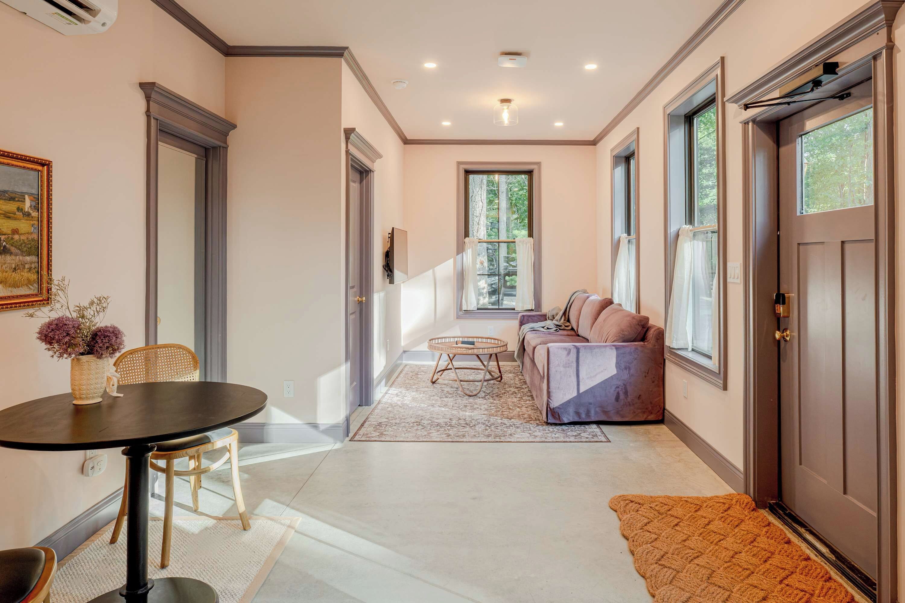 A hallway with a dining area, a sofa, and a large window.