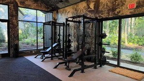 Ett gym med utrustning för styrketräning, stora fönster och utsikt över grönområden.