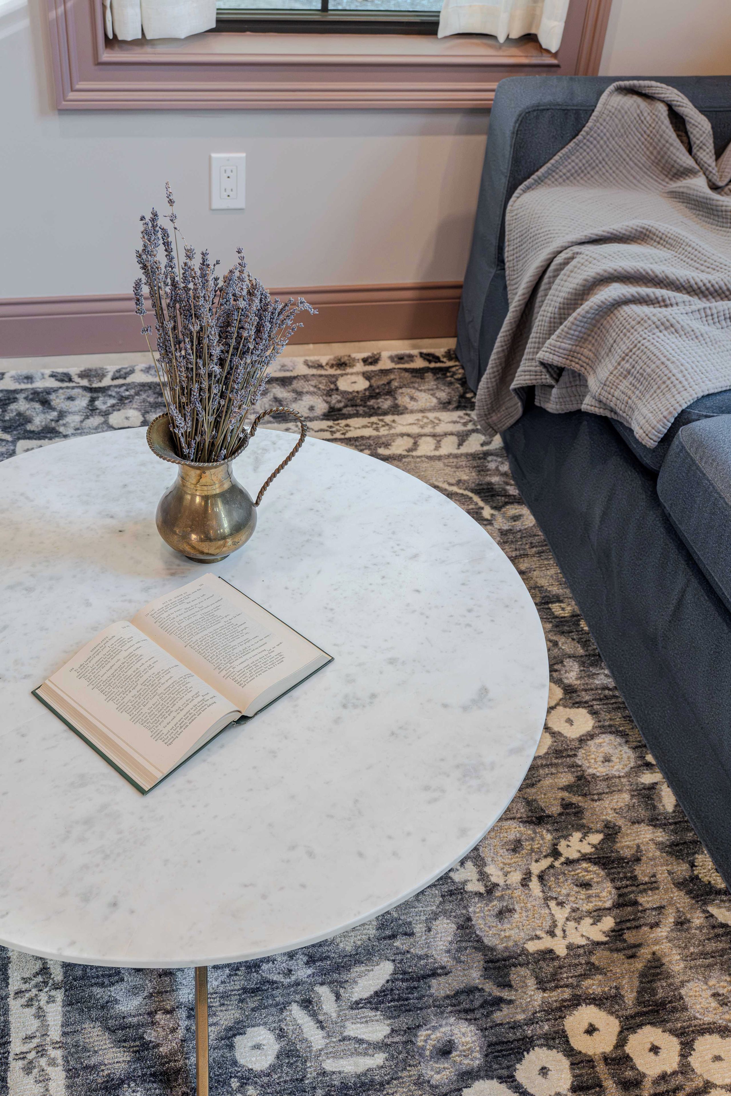 Ein runder Tisch mit einem Buch und einer Vase getrockneter Blumen.