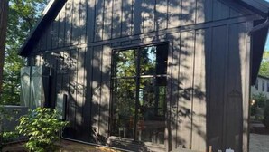 En träbyggnad med en stor glasdörr, en träbänk och en liten trädgårdsyta.