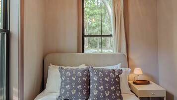 A bedroom with a bed, two pillows, a nightstand with a lamp, and a window with curtains.