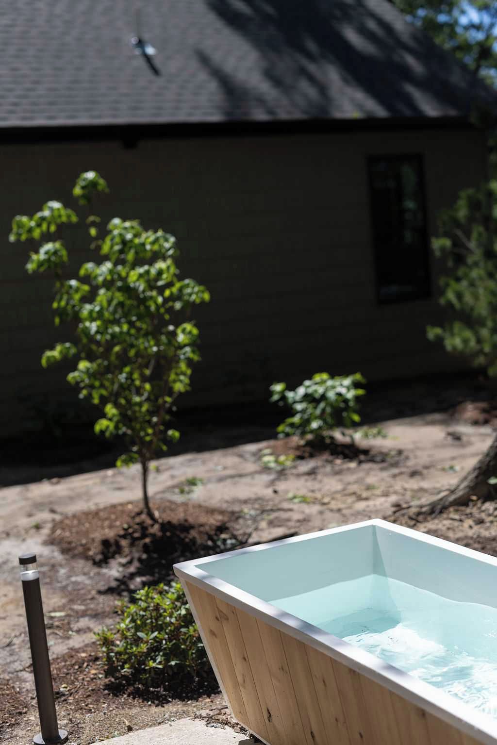 Een houten jacuzzi in een achtertuin, met een huis op de achtergrond.