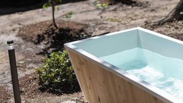 Een houten jacuzzi in een achtertuin, met een huis op de achtergrond.