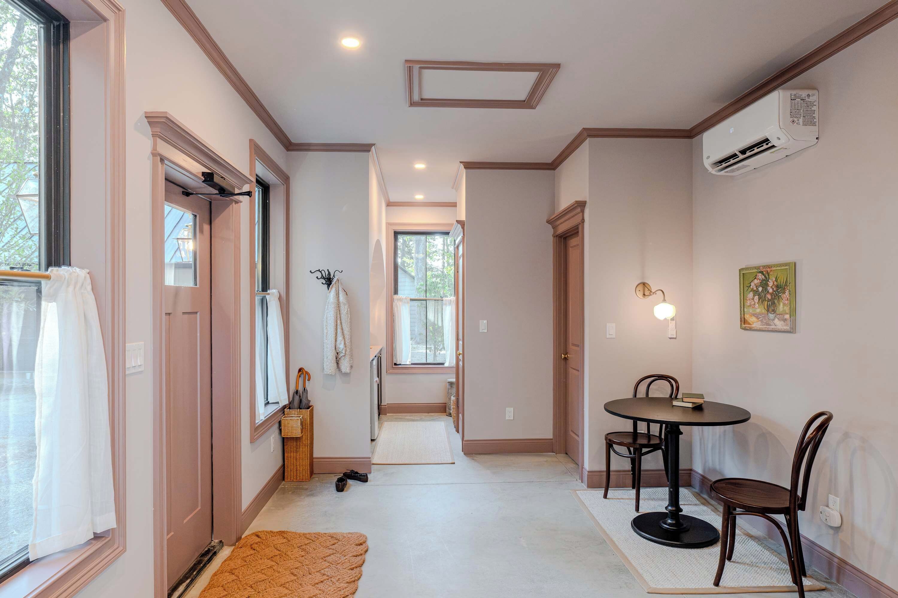 A hallway with a dining area, a coat rack, and a window with a view.