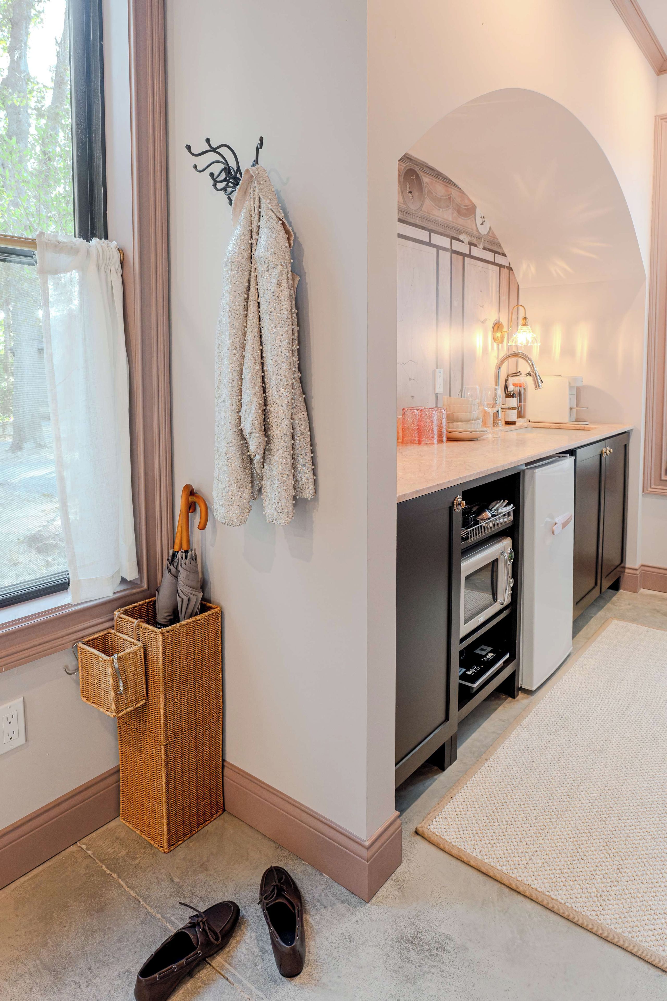Een keuken met een ingebouwde oven, een spoelbak en een aanrecht. Op de vloer staat een rieten mand met schoenen en een paraplu.