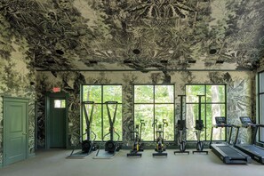 Ett gym med motionscyklar, löpband och annan träningsutrustning, med stora fönster och ett tak som är målat med en växt- och djurmotiv.