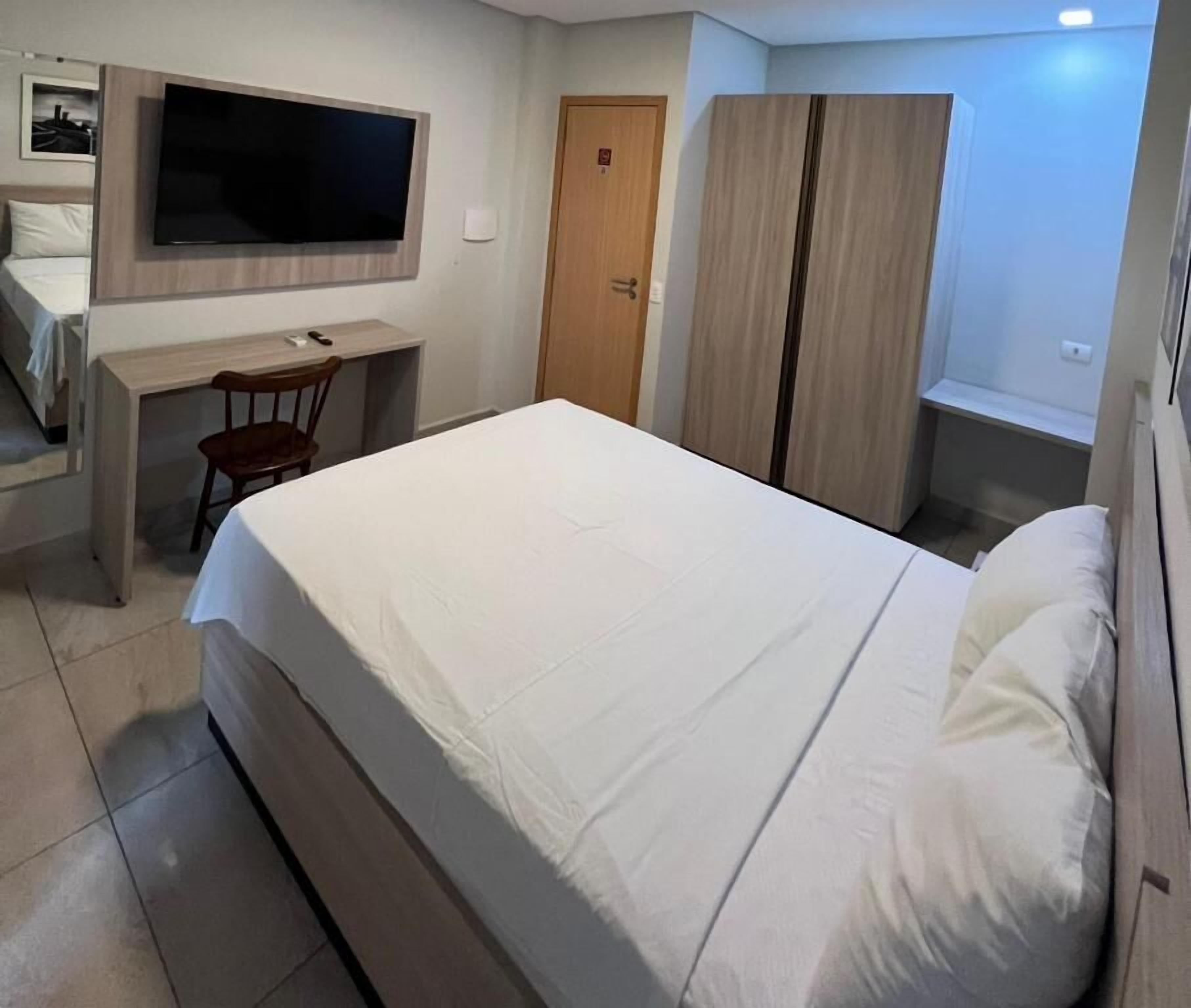 Una camera da letto con un letto, una scrivania, una sedia, un armadio e una televisione.