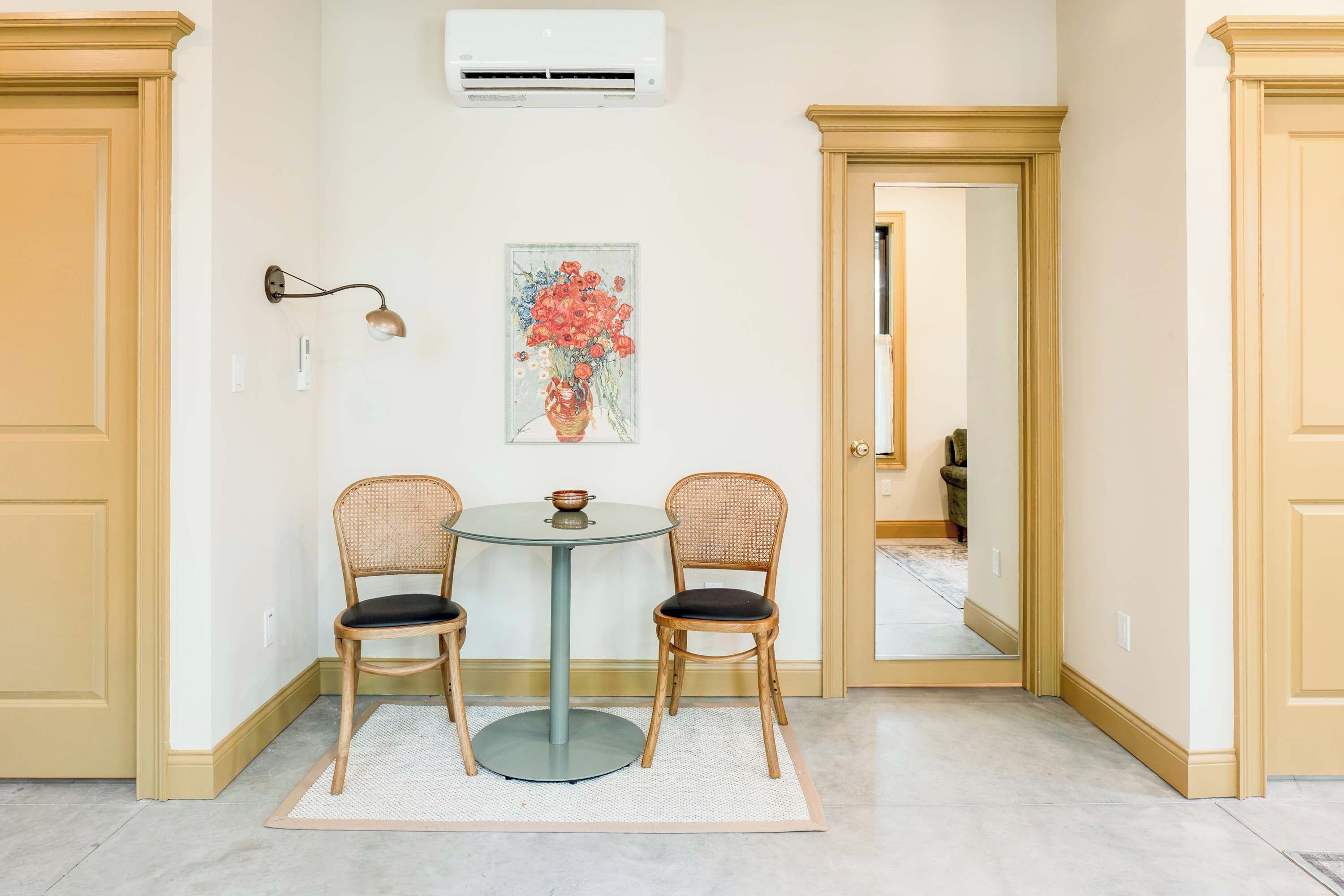 A room with a round table, two chairs, a wall-mounted air conditioner, and a painting.