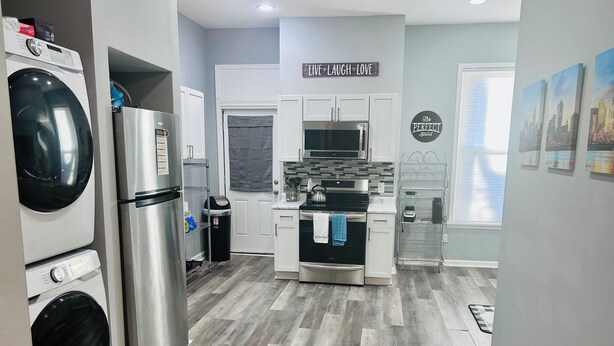 Eine moderne Küche mit einem Edelstahl-Kühlschrank, einem Kombi-Backofen und einer Mikrowelle. An der Wand hängt ein Schild mit der Aufschrift 'LIVE LAUGH LOVE'.