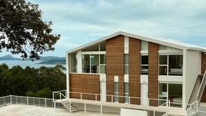 Un moderno edificio de dos pisos con amplios ventanales, un balcón y vista al mar.