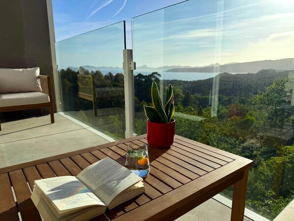 A balcony with a wooden table, a red potted plant, and an open book.