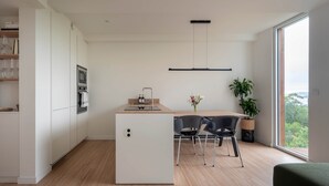 Una cuina moderna amb una illa central, una zona de menjador amb cadires, una finestra gran amb vistes i una làmpada al sostre.