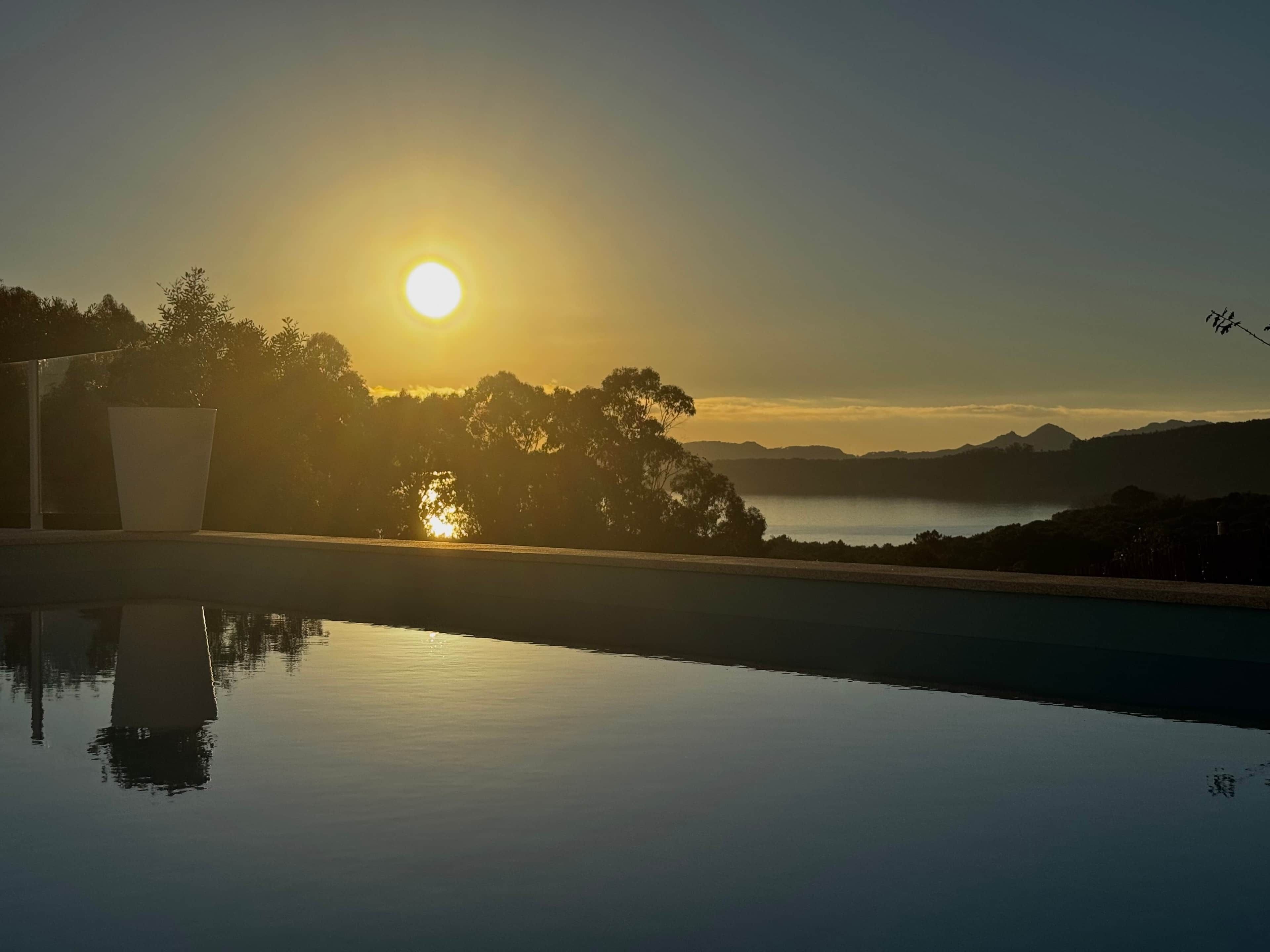 Un coucher de soleil paisible sur un étang tranquille, avec une montagne en arrière-plan.