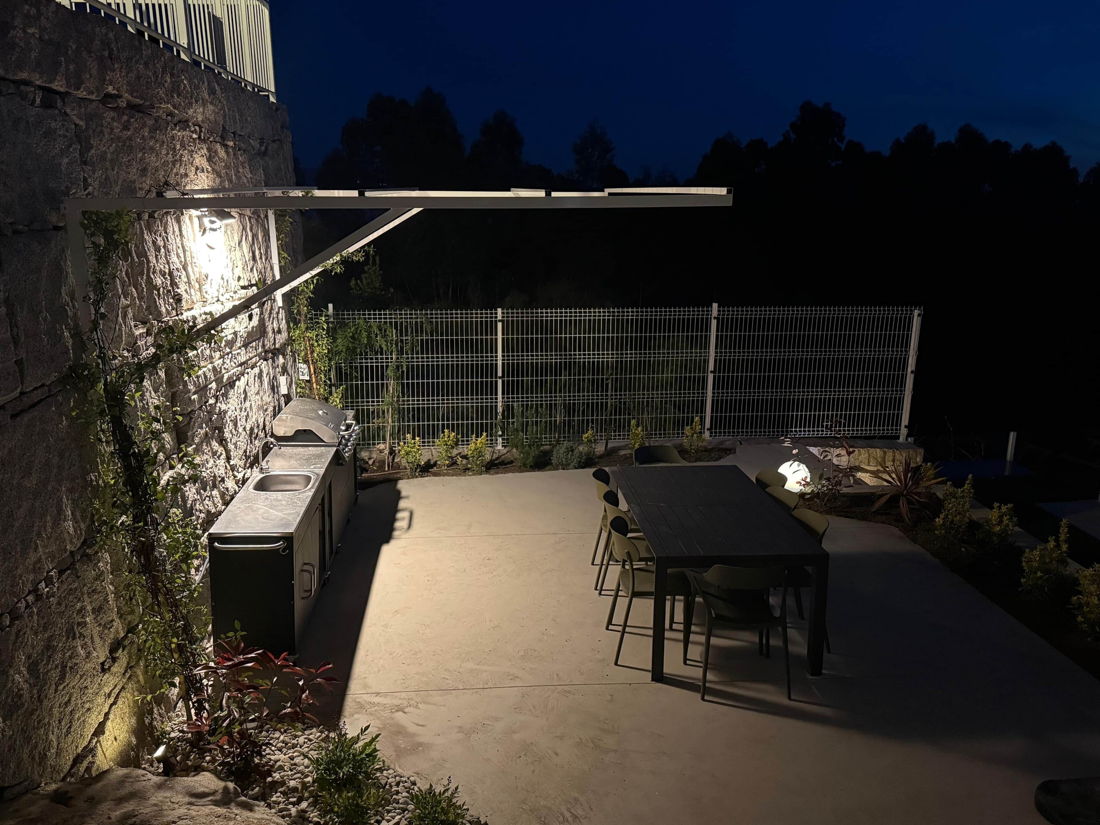 An outdoor patio with a stone wall, a grill, a table, and chairs.